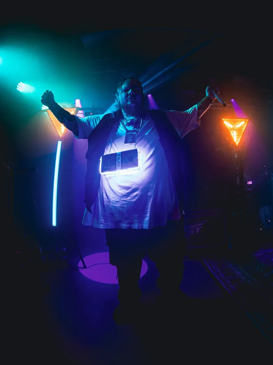 Saenger steht mit ausgebreiteten Armen im cyan und orangenen Gegenlicht