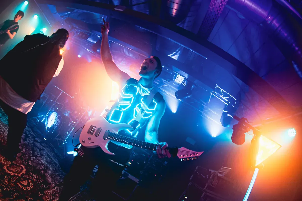 Gitarrist reisst jubelnd den Arm hoch mit leuchtender LED-Weste